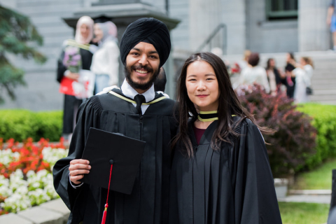 Two students at Convocation in front of Arts building