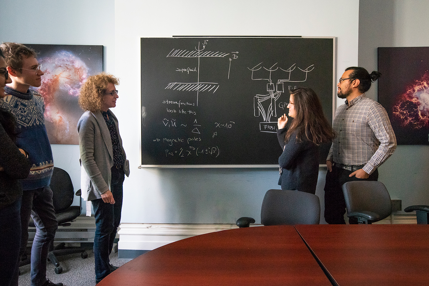 Professor Vicky Kaspi chatting with students in front of a blackboard.